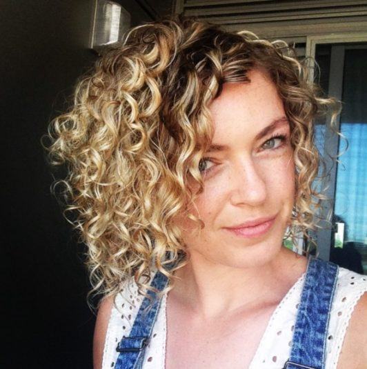 Kręcony blond bob z ciemniejszą nasadą Krótki kręcony bob z blond refleksami i ciemną nasadą